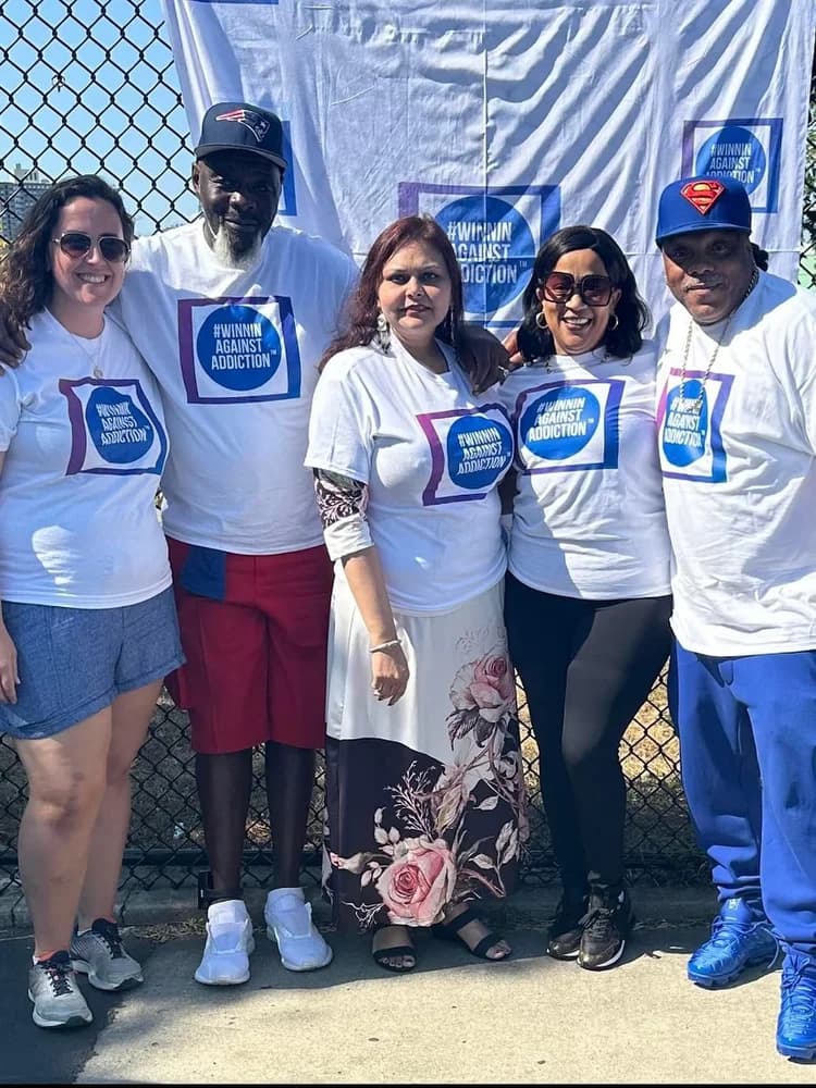 Group of volunteers at Winnin Against Addiction basketball court event with banner in Boston