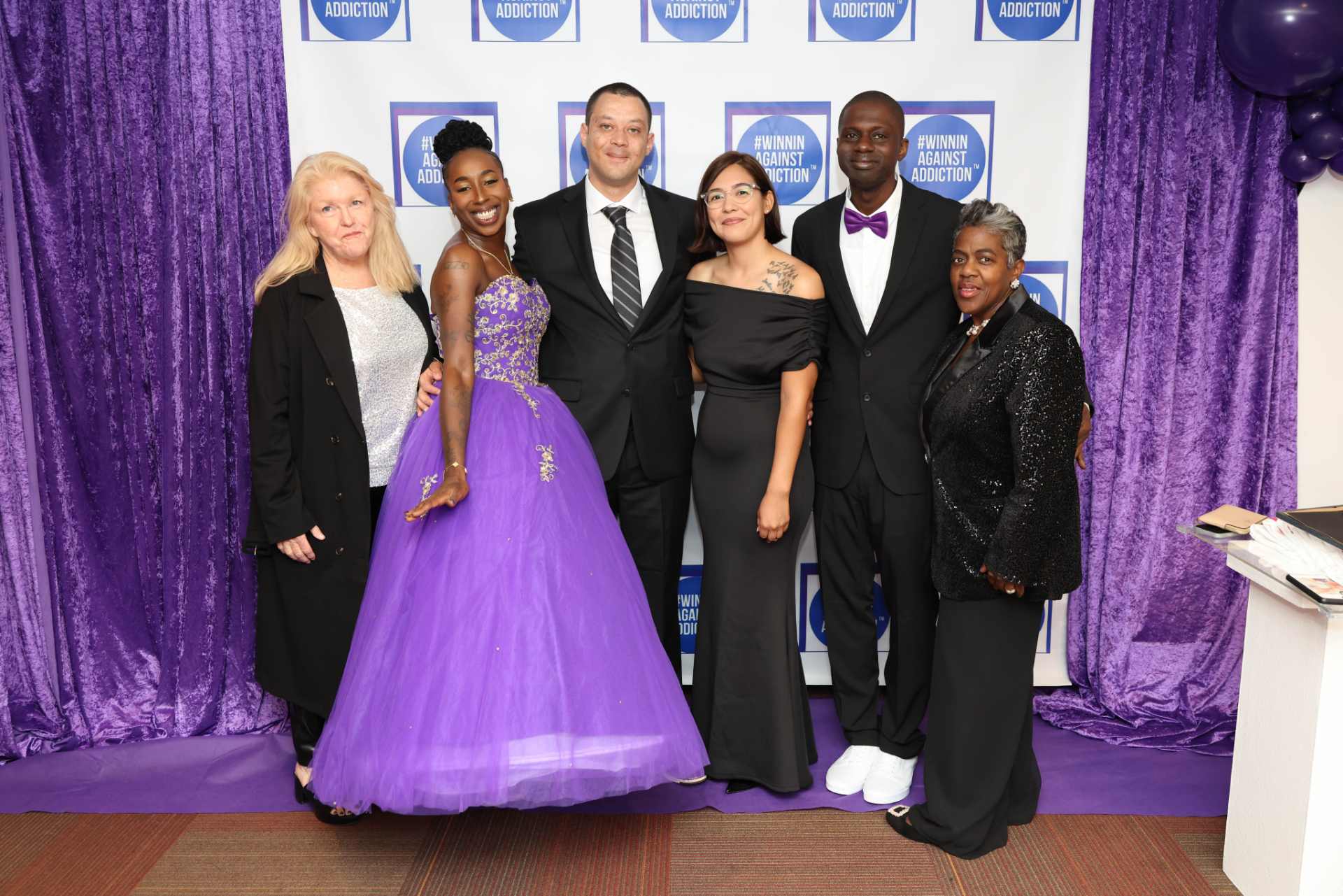 2025 Winnin Against Addiction gala group photo with six people in formal attire on purple carpet