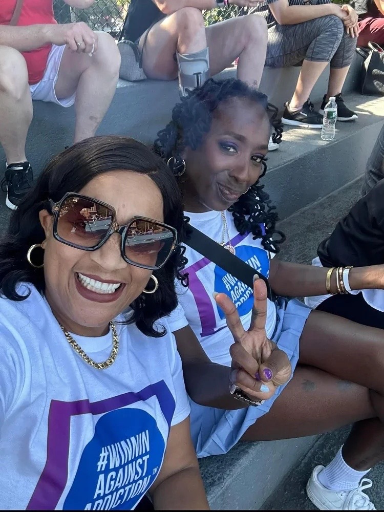 Two women smiling and wearing Winnin Against Addiction shirts during community gathering